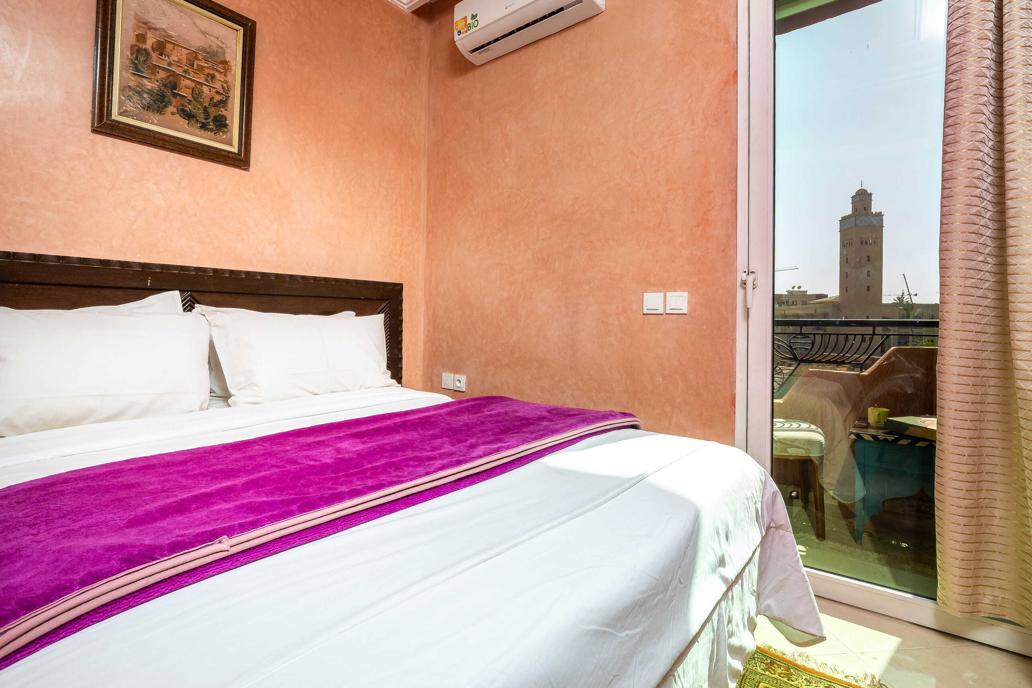 A hotel room with a bed, a window with a view of a tower, and an air conditioning unit.