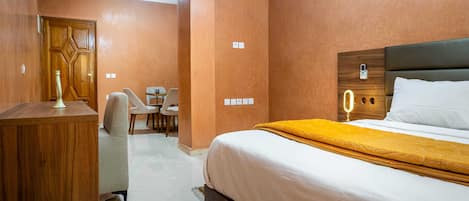 Una camera d'albergo con una scrivania in legno, un letto con copripiumino bianco e giallo, una testiera in legno e un tavolino con sedie.