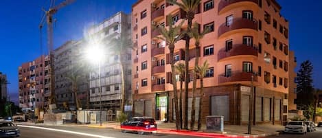 A multi-story building with balconies, palm trees, and a construction crane in the background.