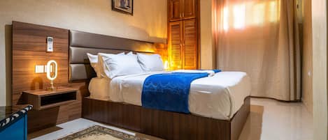 Una camera d'albergo con un letto grande, un comodino, una lampada a parete, un quadro incorniciato e una finestra con tende.