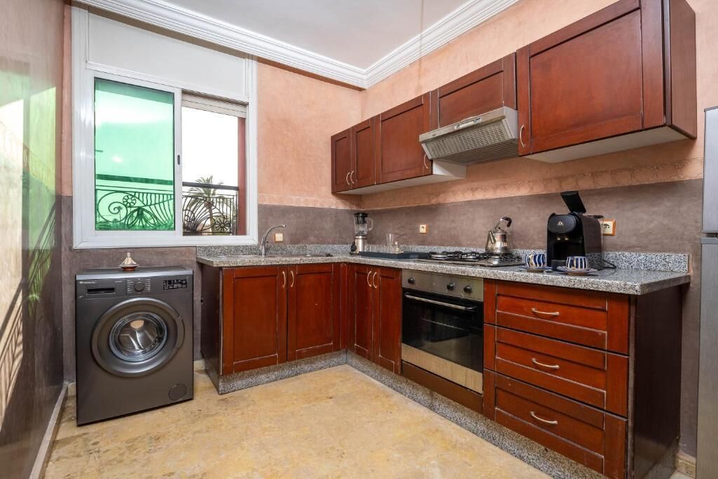 Eine kompakte Küche mit Holzausstattung, einem Einbauofen, einer Waschmaschine und einem Fenster mit Blick auf einen Balkon.