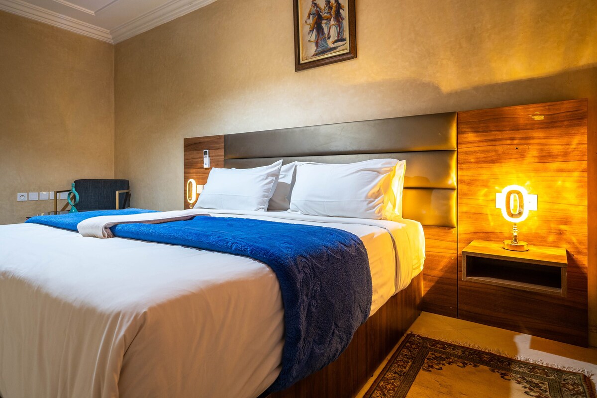 A double bed with white and blue bedding, a nightstand with a lamp, and a wooden headboard.