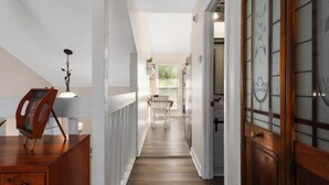 Un pasillo con piso de madera, barandal blanco y una puerta con panel de vidrio.