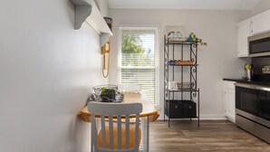 Una cocina con una mesa de madera, una silla blanca y un estante metálico negro.
