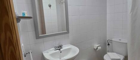 A bathroom with white tiles, a sink, a toilet, and a shower curtain.