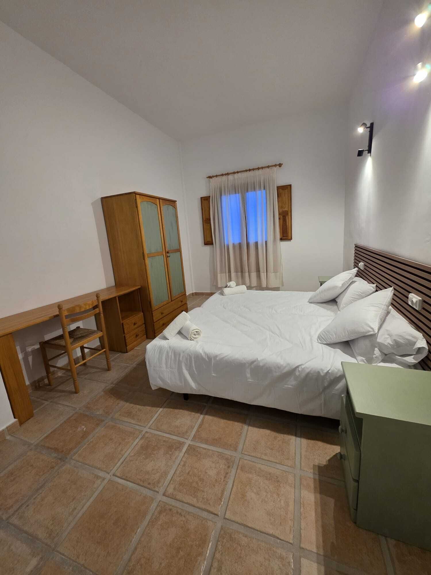 Un dormitorio con cama, escritorio, armario y ventana con cortinas.