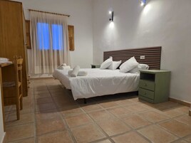 Una habitación de hotel con una cama, dos mesitas de noche, un armario de madera y una ventana con cortinas.