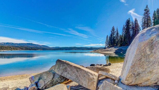 Un lago transparente con una orilla rocosa y árboles al fondo.