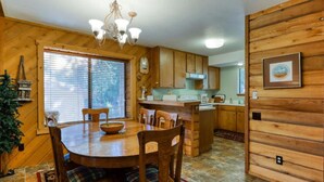 Un interior de madera con una mesa de comedor, sillas, una araña y una zona de cocina.