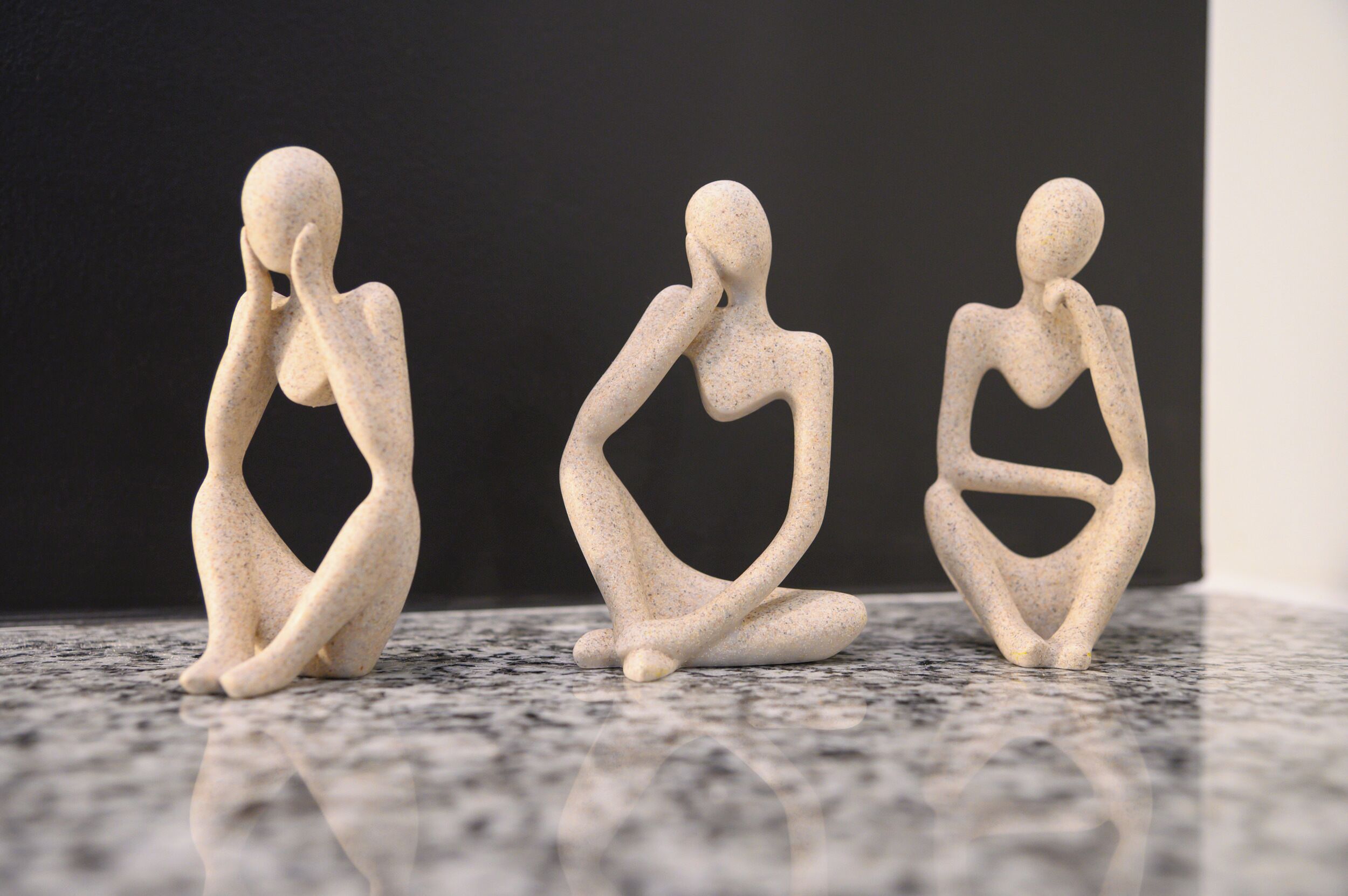 Three abstract sculptures on a granite floor against a dark background.