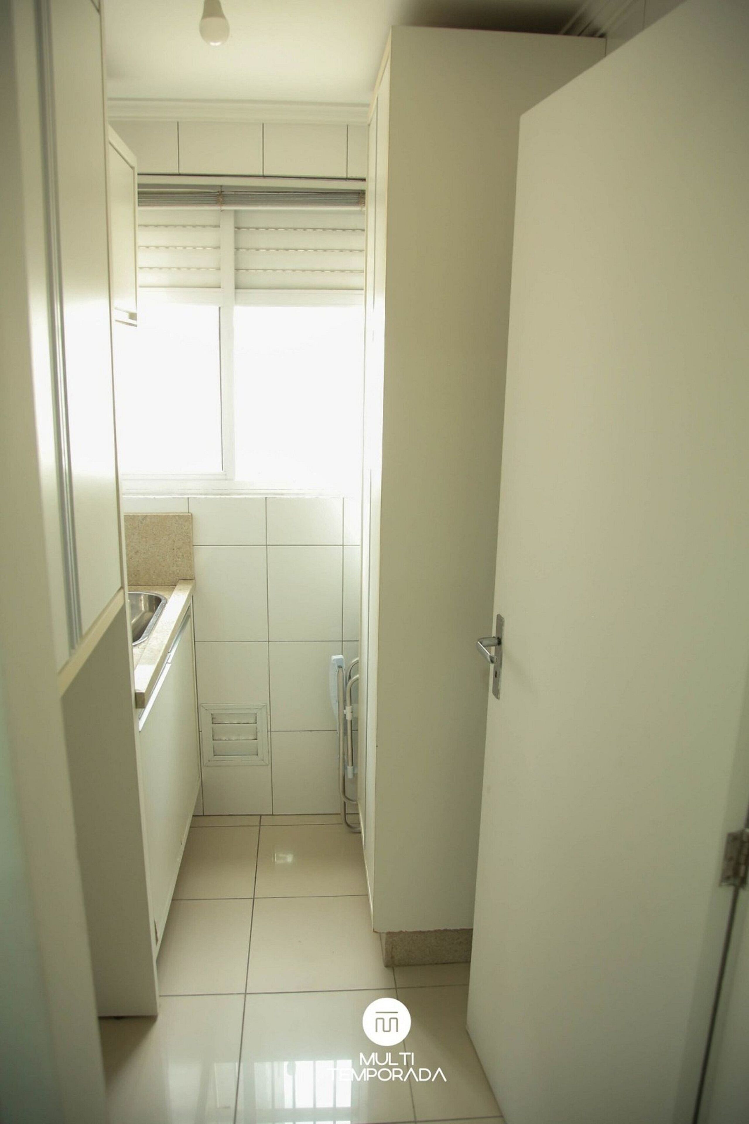 Un pasillo estrecho que desemboca en una zona de cocina, con una ventana, un fregadero y una puerta.