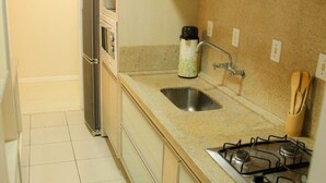 A compact kitchen with a gas stove, sink, and a refrigerator. - Apartamento Centro de Imbituba - SC (Imbituba)