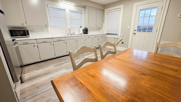 Una cocina con armarios blancos, una mesa de comedor de madera y un microondas.