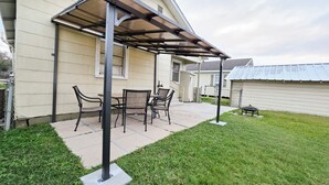 Un patio con mesa y sillas, una zona techada y un césped.