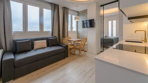 A modern living room with a sofa, dining table, and chairs, a kitchen area with a sink and countertop, and a TV mounted on the wall. - GRAN VIA capitals, LiSBOA (Madrid)