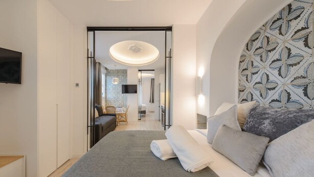 A modern bedroom with a large bed, a TV mounted on the wall, and a patterned headboard. - GRAN VIA capitals, LiSBOA (Madrid)