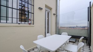 A balcony with a white table and chairs, a window with metal bars, and a view of a cityscape. - GRAN VIA capitals, LiSBOA (Madrid)