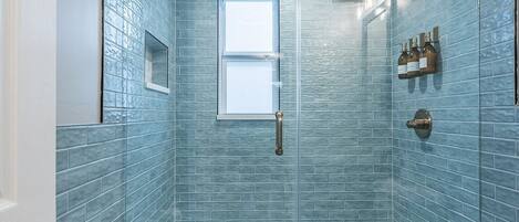 A bathroom with blue-tiled walls, a window, a towel rack, and a toilet.