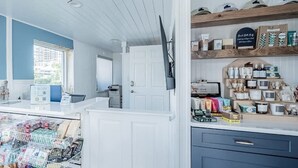 Myymälätila, jossa on myyntitiski, tuotteilla täytettyjä hyllyjä ja ovi, joka johtaa toiseen huoneeseen.