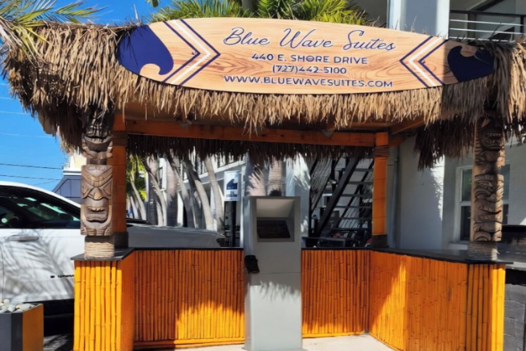 A wooden sign for Blue Wave Suites with contact information and website URL.