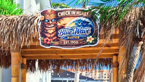 Schild von Blue Wave Suites mit tropischem Design, Holzbauweise und einer Palme.