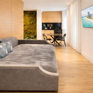 A modern bedroom with a large gray sofa, a dining area with a small table and chairs, and a kitchen in the background. - Relaxing Studio Retreat in Miami Beach (Miami Beach)