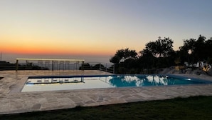 A rectangular swimming pool with a stone deck, surrounded by chairs and a railing, set against a sunset backdrop. - Domaine de Filia (Aalali)