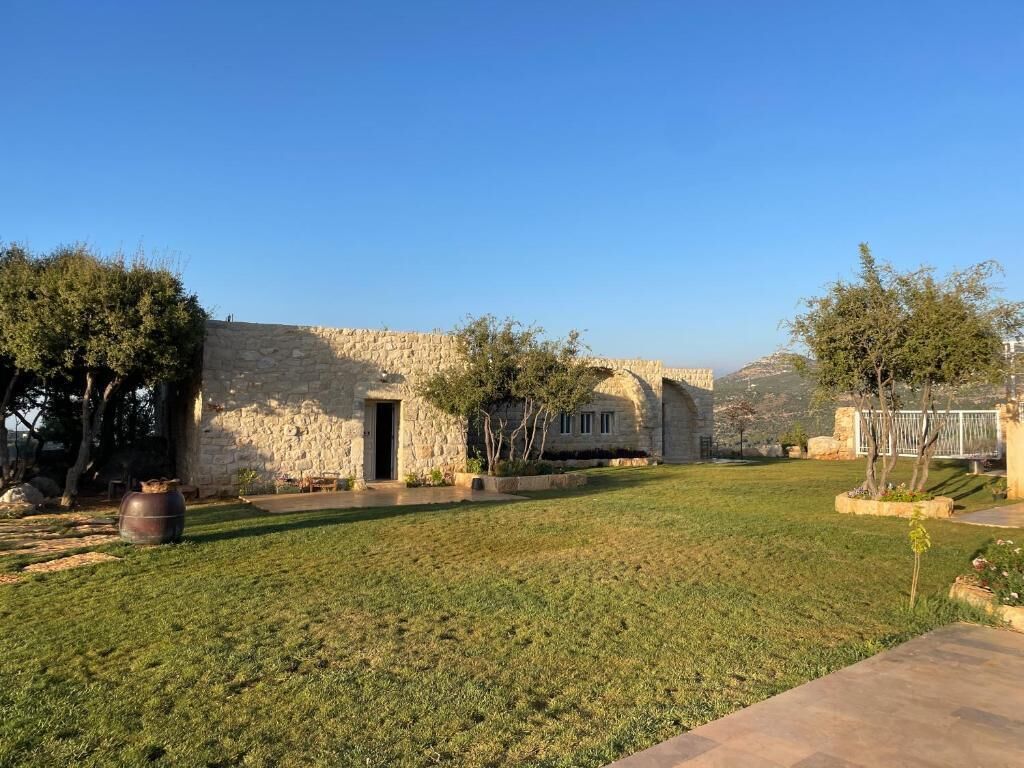 A stone building with a grassy courtyard, a stone wall, and trees.