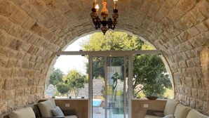 A stone-walled room with a glass door leading to a pool, furnished with two sofas and a coffee table. - Domaine de Filia (Aalali)