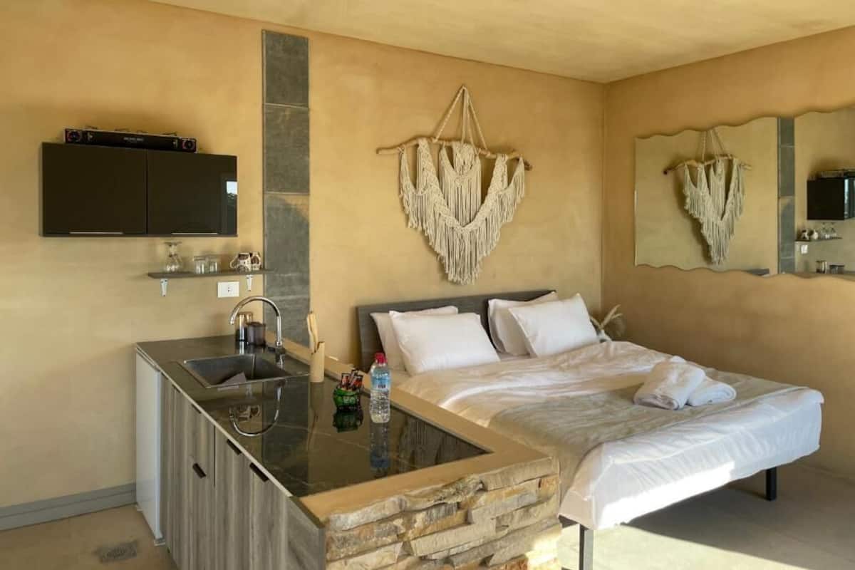 Habitación de hotel con cama, lavamanos integrado, televisor de pantalla plana y decoración de pared en macramé.