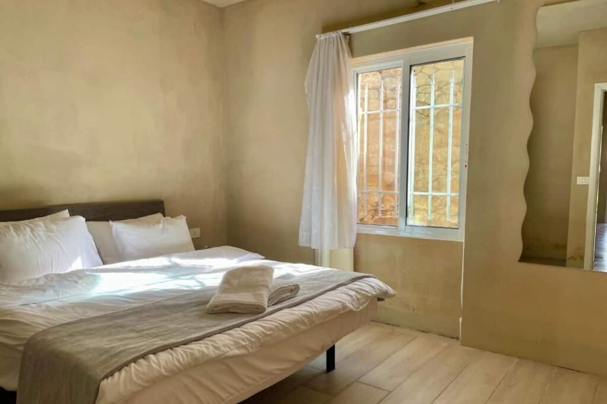 Un dormitorio con cama, cortinas en la ventana y un espejo en la pared.