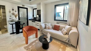 Ein modernes Wohnzimmer mit einer Couch, einem Couchtisch und einem Essbereich, im Hintergrund befindet sich eine Küche.