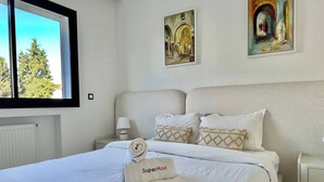 Ein ordentlich bezogenes Bett mit Handtuch von einem Superhost, ein Nachttisch mit Lampe und zwei Bilder an der Wand.
