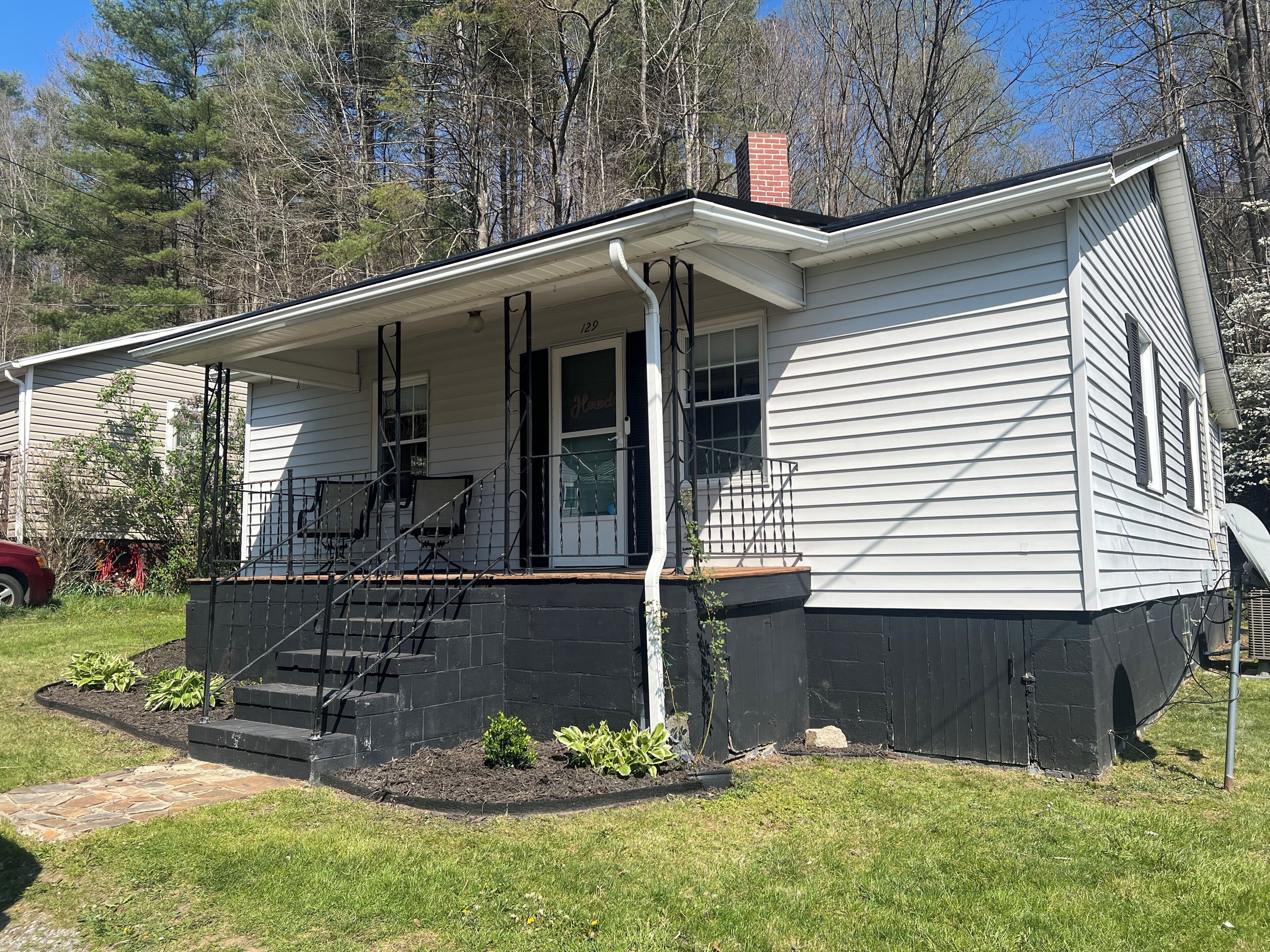 A single-story house with a front porch, a visible number '129' on the door, and a brick foundation.
