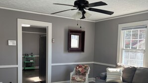 Un salon avec un ventilateur de plafond, une fenêtre, un canapé, un tapis à motifs et un fauteuil.