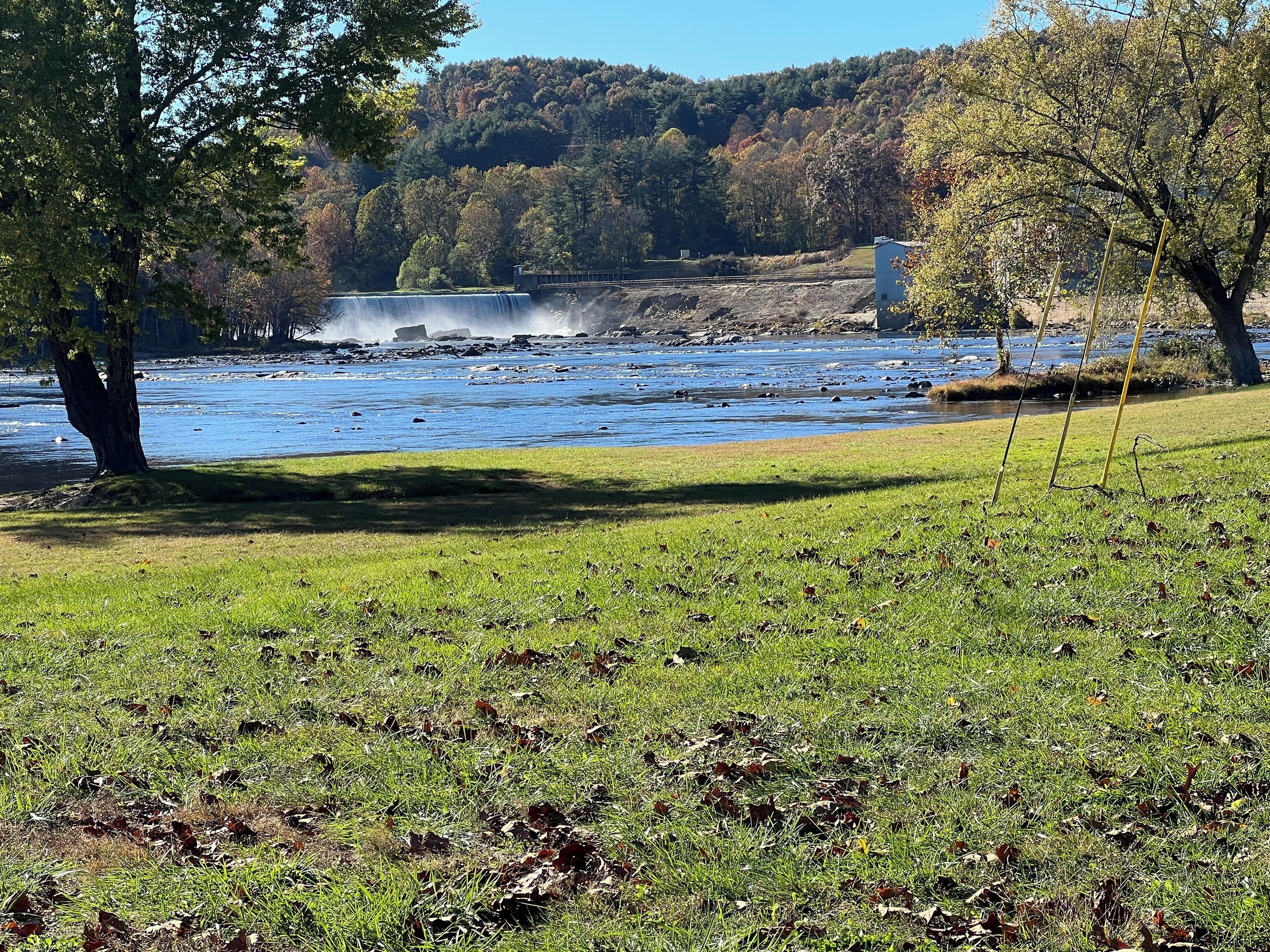 A river with a waterfall, surrounded by grassy areas and trees.