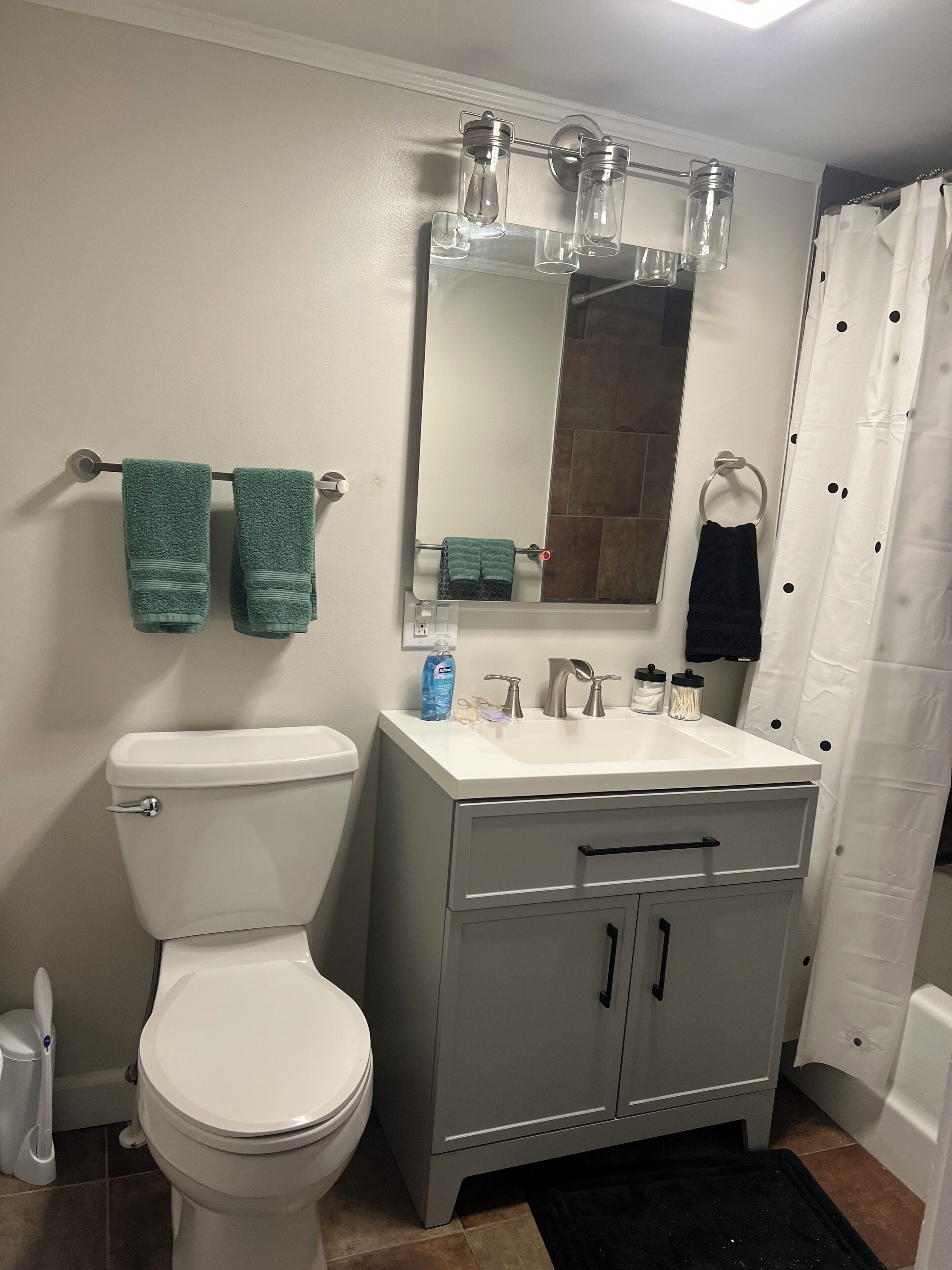 A bathroom with a toilet, sink, and mirror. There are towels hanging on a rack and a shower curtain.