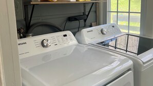 Un espace dédié à la lessive, avec une bouteille de lessive jaune, un lave-linge Samsung et un sèche-linge Samsung.
