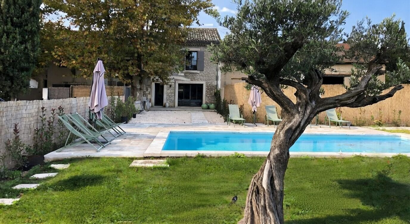 A poolside area with a stone building, a tree, and outdoor seating.