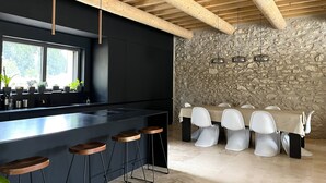 Una cucina moderna con una grande isola, sgabelli da bar e un'area pranzo con sedie bianche e una parete in pietra.