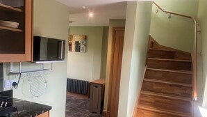 A kitchen with wooden cabinets, a black countertop, and a microwave. There is a staircase with wooden steps leading to another room. - Kick back and relax in this calm, stylish with views of beautiful Strathnairn. (Inverness)