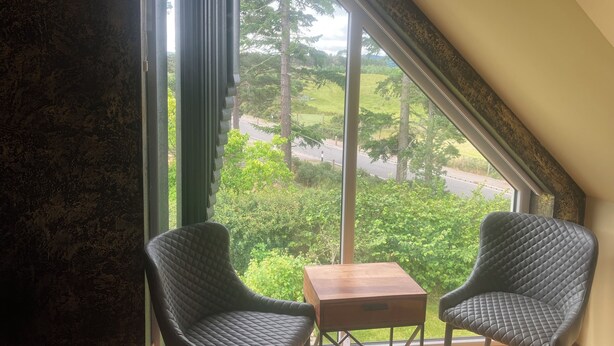 A room with two chairs and a small table, large windows with a view of greenery and a road, and a sloped ceiling. - Kick back and relax in this calm, stylish with views of beautiful Strathnairn. (Inverness)