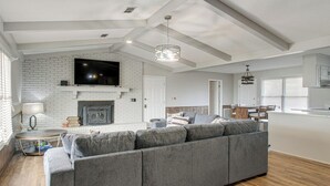 A spacious living area with a fireplace, a large flat-screen TV, a sofa, and a dining area with a table and chairs. - Pond View, Fishing, BBQ, Fireplace, and More (Douglas)