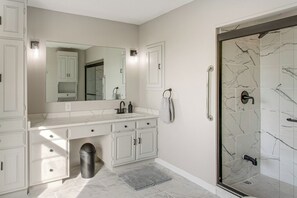A bathroom with a white vanity, a large mirror, a shower with marble tiles, and a trash can. - Pond View, Fishing, BBQ, Fireplace, and More (Douglas)