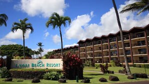 Un resort con un cartel que dice 'Lahaina Beach Resort', con un edificio de varios pisos con balcones, rodeado de palmeras y jardines tropicales.