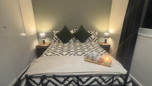 Uma cama bem arrumada com um cobreleito estampado, dois travesseiros e uma bandeja com uma vela e duas xícaras.