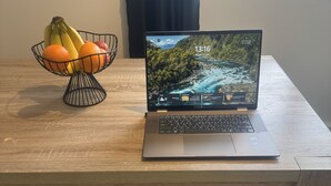 Um laptop sobre uma mesa de madeira, com uma fruteira ao lado.