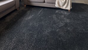 Uma sala de estar com um sofá cinzento, um abajur e uma obra de arte floral emoldurada na parede.