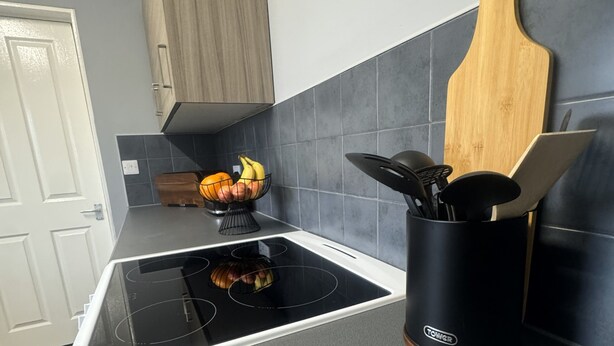 Uma cozinha com um fogão por indução preto, uma tábua de corte de madeira e um suporte para facas preto.