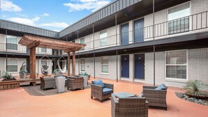 Une cour dotée d’un espace extérieur aménagé avec des sièges, d’une pergola et d’un bâtiment en briques comportant de nombreuses fenêtres et portes.